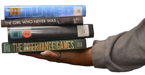 Kelani Cruz holds up the four books from the quiz. The books include: Muted by Tami Charles, The Girl Who Never Was by Skylar Dorset, The Unbecoming of Mara Dyer by Michelle Hodkin, and The Inheritance Games by Jennifer Lynn Barnes.