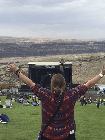 Teacher Allison Haley throws her hands up in front of a concert's stage. She's in the crowd to see her favorite band, Dave Matthew's Band play.