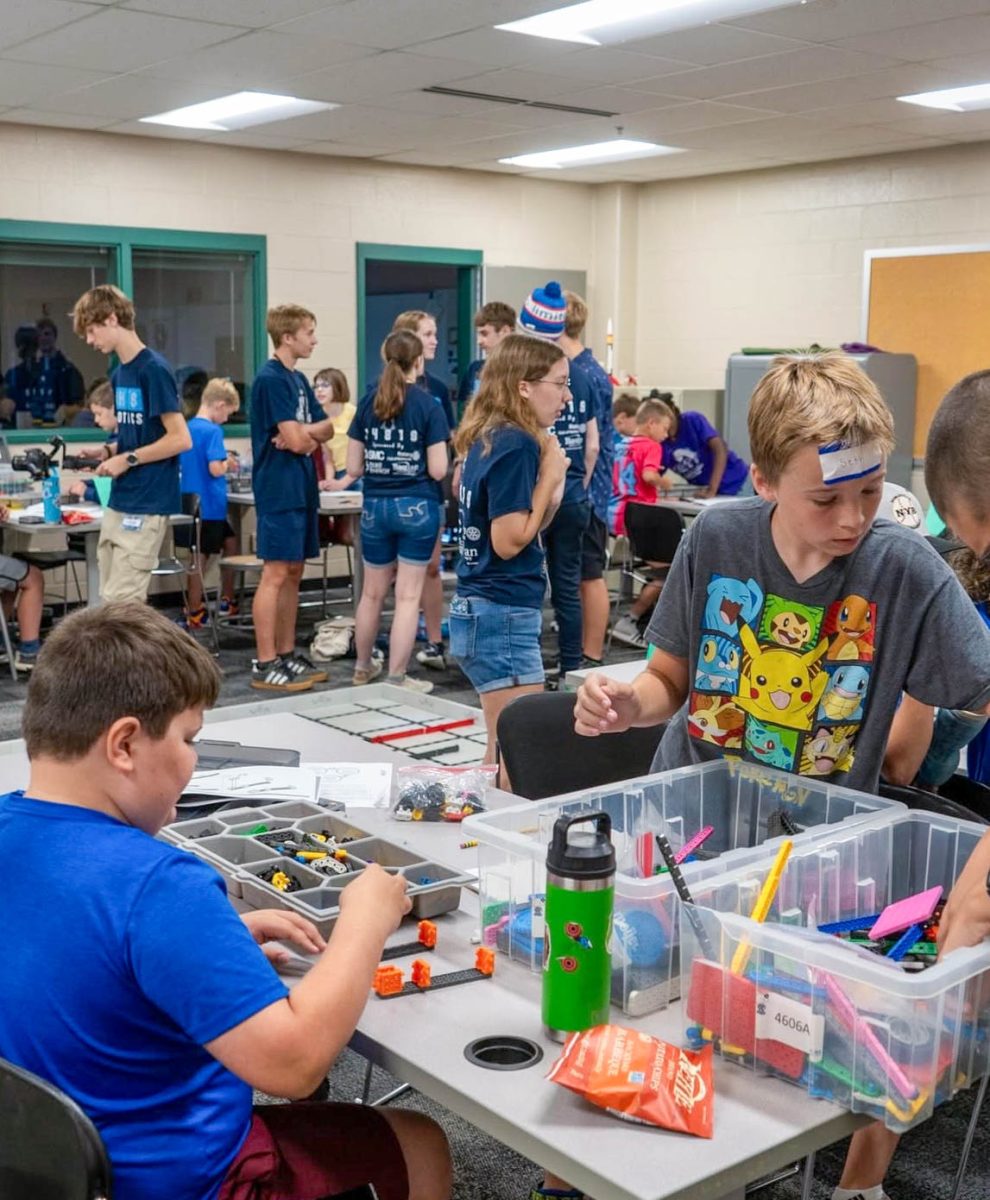 Elementary kid preparing for a robotics competition under the watchful eyes of the high school robotics team.